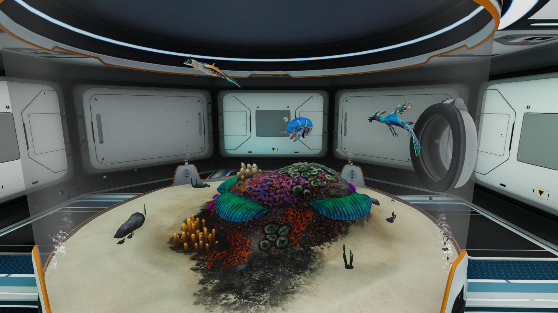 Subnautica Below Zeroの拠点内に設置された大型水槽。砂地や色鮮やかな植物の周囲を複数の海洋生物が泳いでいる